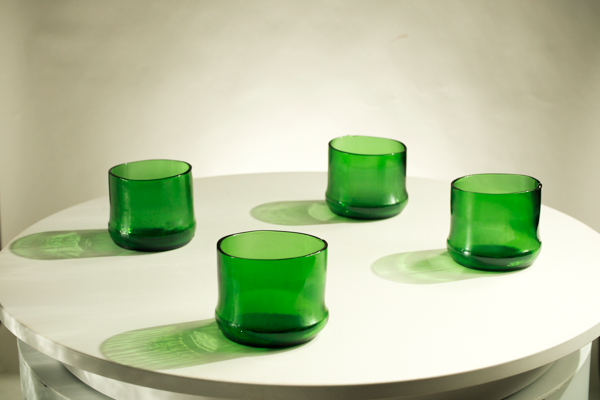 Four translucent green glass tumblers arranged on a round white table against a light neutral background.