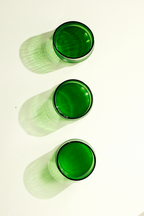 Three green tinted glass shot glasses arranged vertically on a white background, casting soft green shadows.