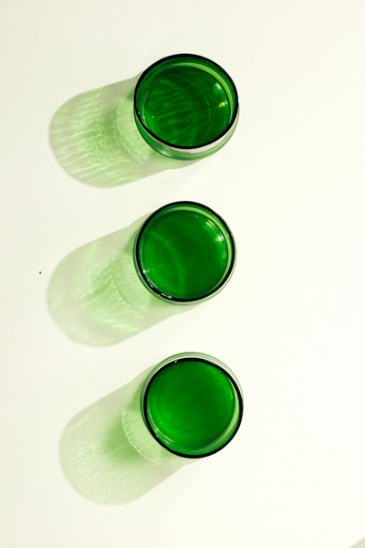 Three green tinted glass shot glasses arranged vertically on a white background, casting soft green shadows.